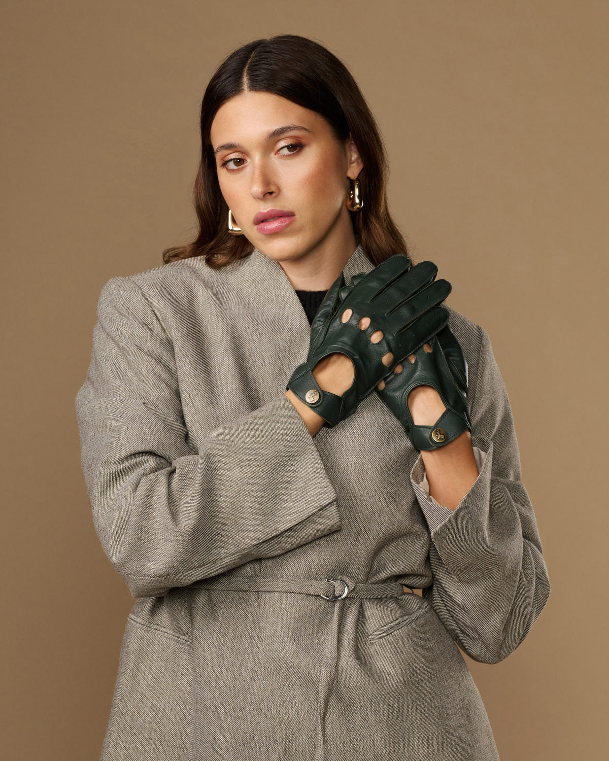 Dark green leather driving gloves with five-finger cutouts and round gold emblems