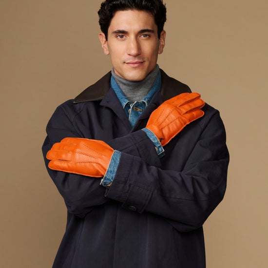 Men’s orange leather gloves with blue lining cuff, arms crossed