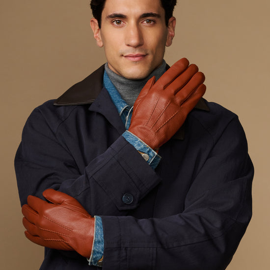 Cognac leather gloves with blue wool lining cuff, one hand raised