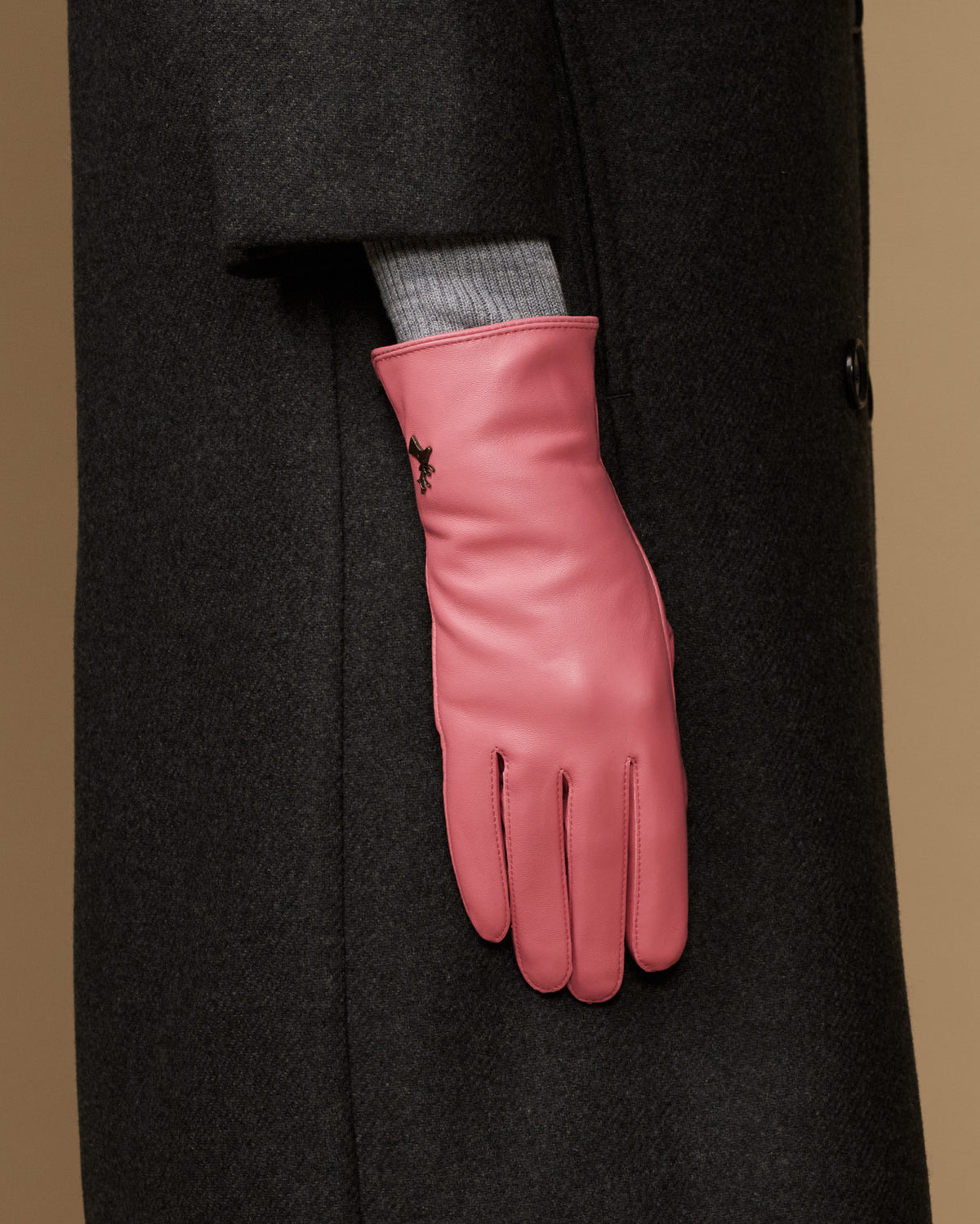 Women’s pink leather glove on a coat sleeve, showing wrist seam and finger stitching