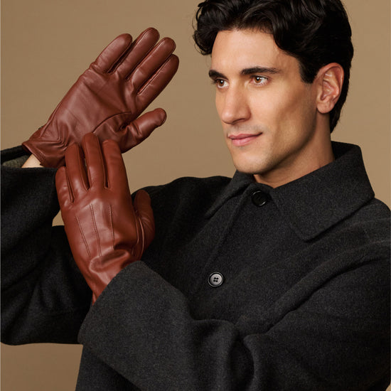 Cognac leather gloves with fleece-lined cuffs, model holding one glove raised