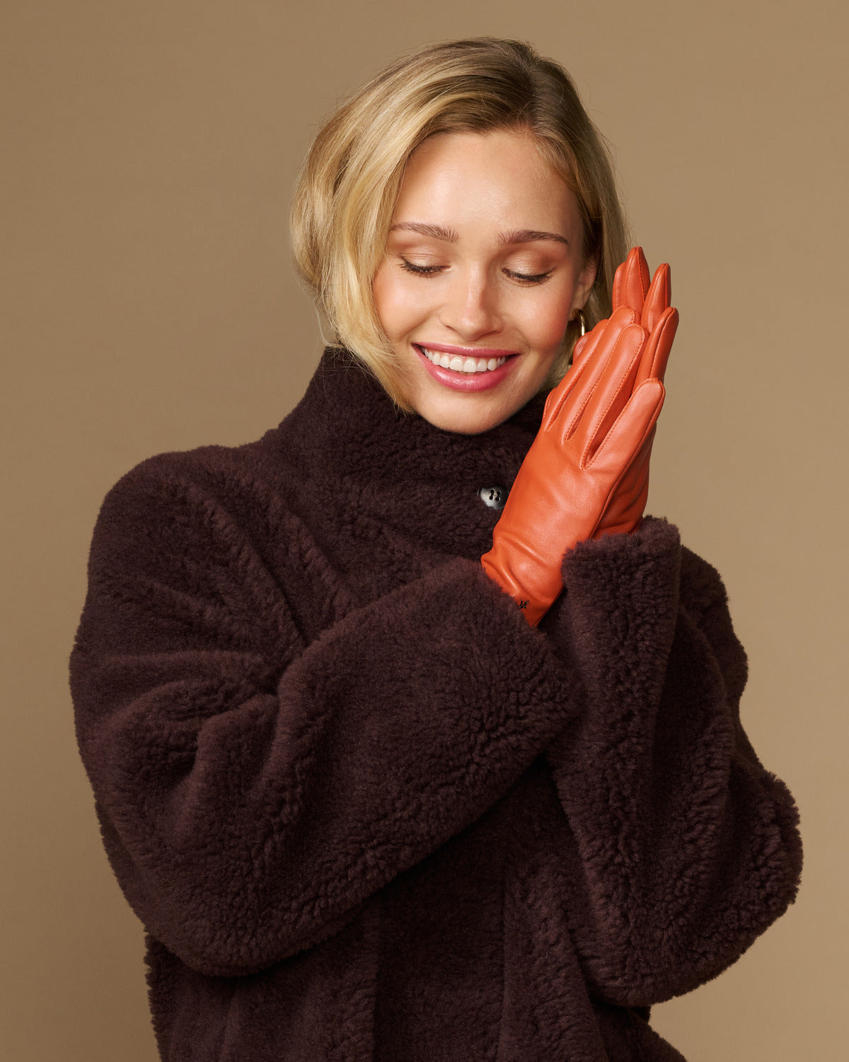 Lauren orange lambskin leather gloves with touchscreen tips, silk-lined, posed on hands
