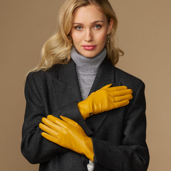 Yellow leather gloves with stitched knuckles, fitted wrist cuff, and small emblem detail