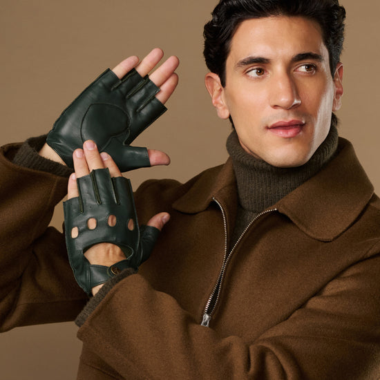 Dark green lambskin driving gloves with fingerless tips and perforated knuckles, worn on both hands