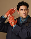 Men's orange fingerless lambskin driving gloves worn with denim cuff and snap tab