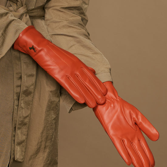 Orange sheepskin leather glove laid across a jacket sleeve, showing stitched fingers
