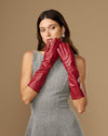 Red below-elbow leather gloves held together near face, showing glossy leather texture