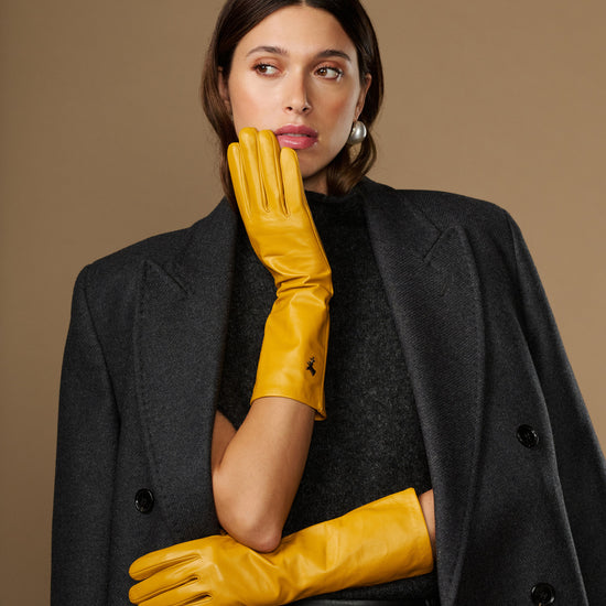 Yellow mid-forearm leather gloves with smooth sheen and stitched knuckle area