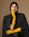 Yellow mid-forearm leather gloves with smooth sheen and stitched knuckle area