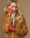Orange fingerless driving gloves on model, thumb and finger cutouts with wrist strap