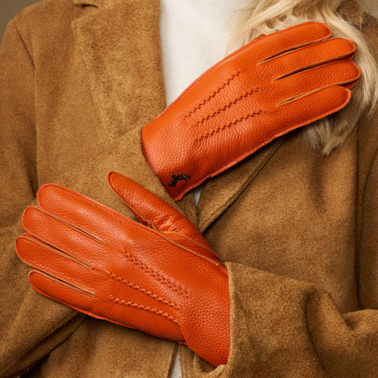 Orange leather gloves with stitched seams and soft lined cuffs, shown folded over sleeve